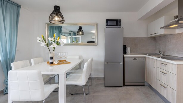 Eine moderne Küche mit Kühlschrank, Mikrowelle und Geschirrspüler. Ein Esstisch mit Stühlen und eine Vase mit Blumen sind ebenfalls vorhanden.