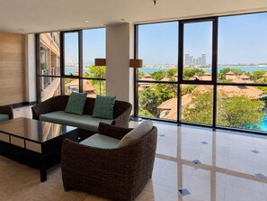 A spacious balcony with a sofa and chairs, large windows offering a view of a coastal area.