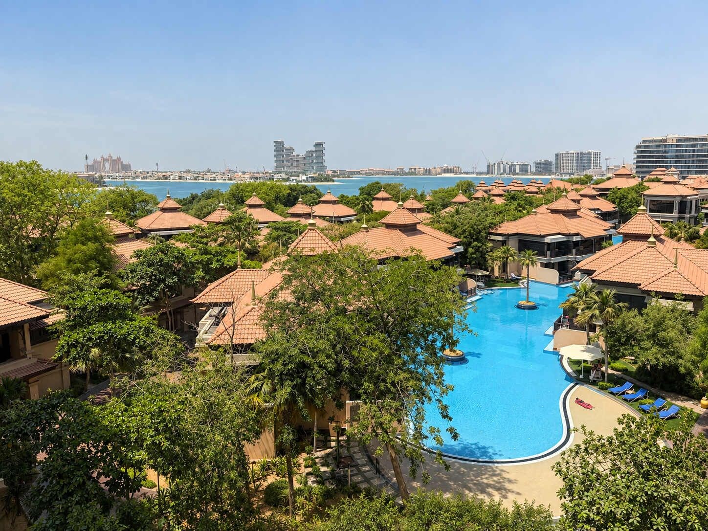 Un complejo turístico con piscina central rodeada de villas con tejados rojos.