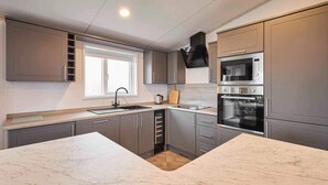 A modern kitchen with grey cabinets, a large marble island, a built-in oven, and a window providing natural light. - Host Stay Linden Lodge Ashdown Retreat (Pickering)