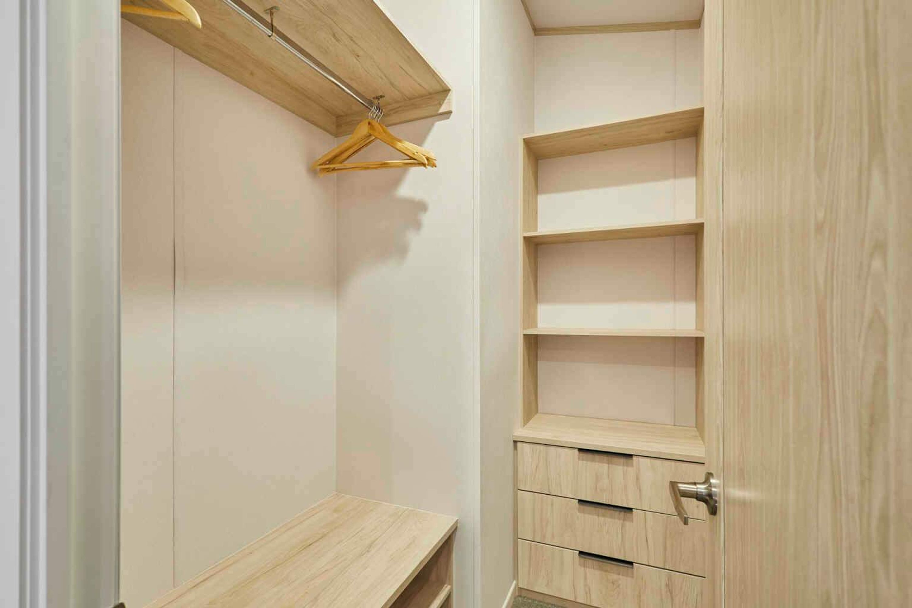 Un vestidor con estantes y cajones de madera, una barra para colgar ropa y un banco.