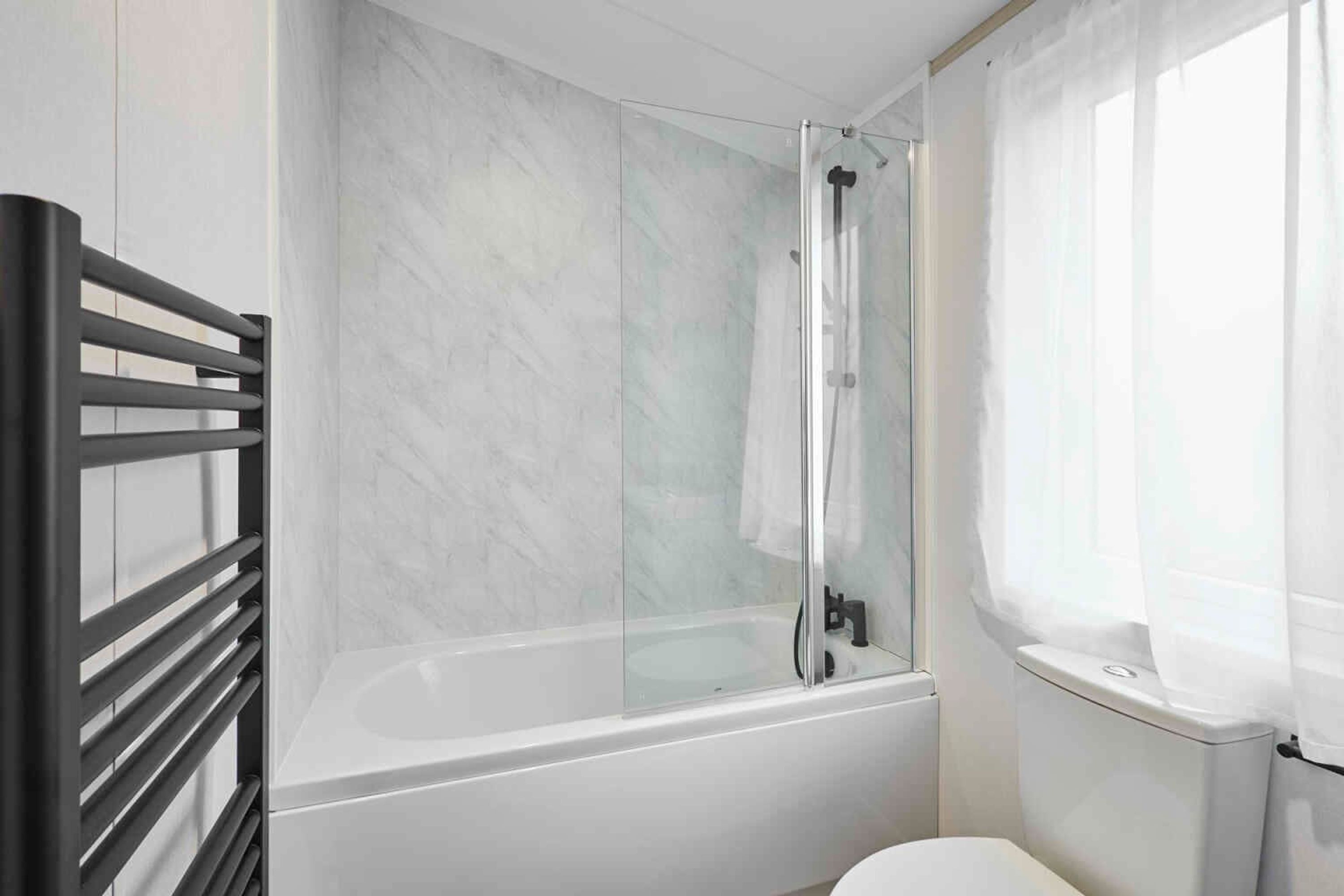 A modern bathroom with a glass-enclosed shower, a white bathtub, and a toilet.
