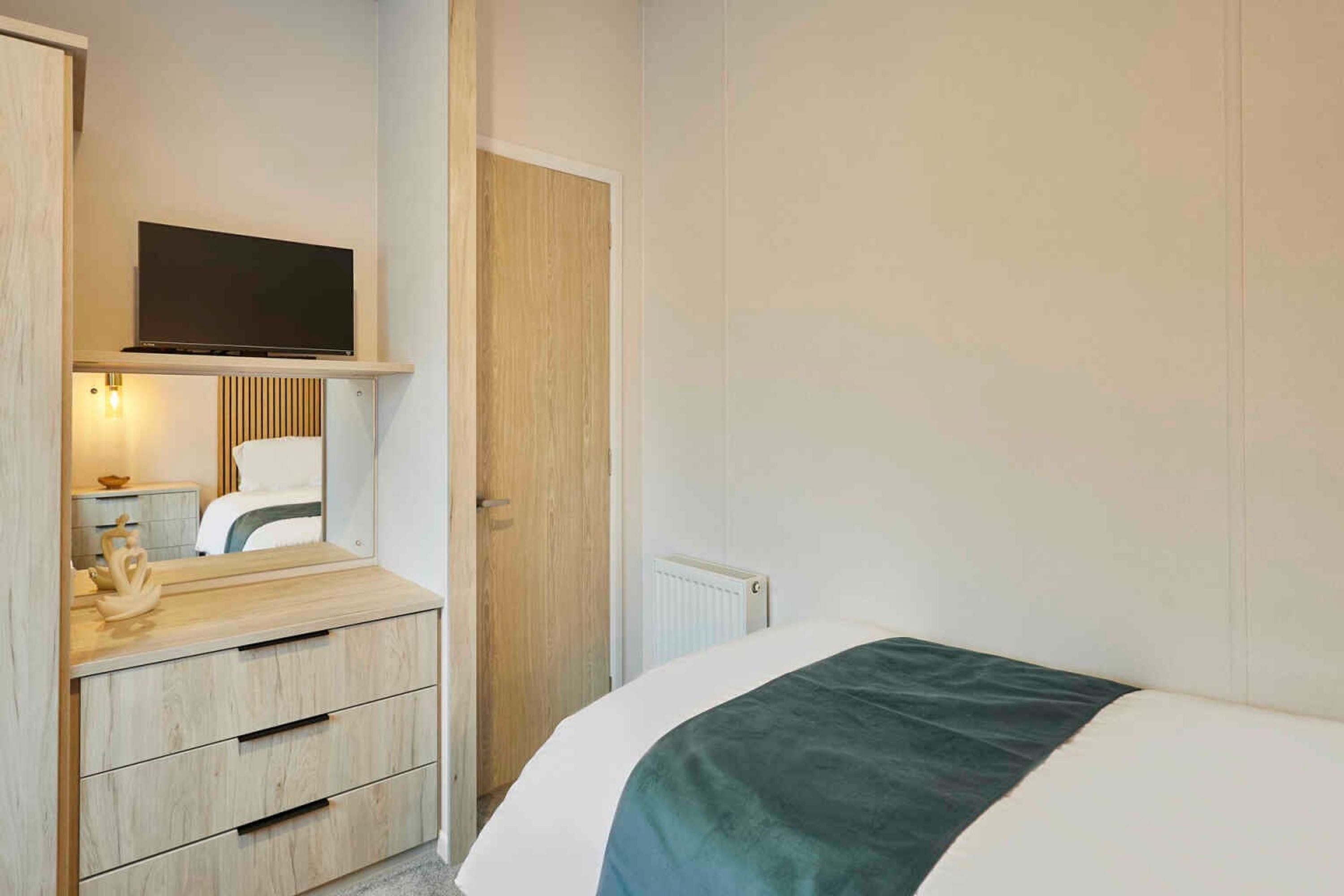 Une chambre à coucher avec un lit, un téléviseur fixé au-dessus d’une commode et une porte.