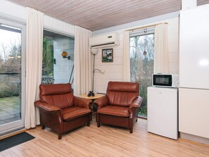 A room with two leather chairs, a small table, a white refrigerator, and a window with curtains. - 6 Person Holiday Home in Herning (Herning)
