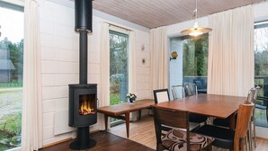A cozy room with a wood-burning stove, a dining table with chairs, and large windows offering a view of the outdoors. - 6 Person Holiday Home in Herning (Herning)