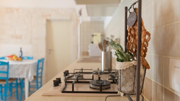 A kitchen with a gas stove, a hanging plant, and a blue table with chairs. - Villa in Itria Valley With Infinity Pool (Cisternino)