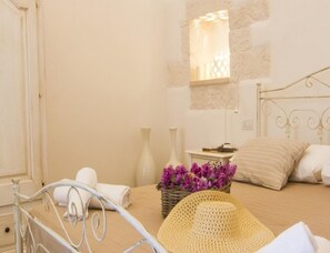 A bedroom with a bed, a bedside table, a lamp, a vase with flowers, and a straw hat on the floor. - Villa in Itria Valley With Infinity Pool (Cisternino)
