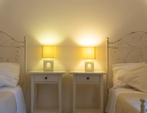Ein Schlafzimmer mit zwei Einzelbetten, jeweils mit weißem Kopfteil und einem Nachttisch mit Lampe.