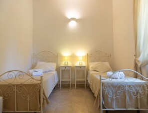 A room with two single beds, each with a nightstand and a lamp, and a ceiling light fixture. - Villa in Itria Valley With Infinity Pool (Cisternino)