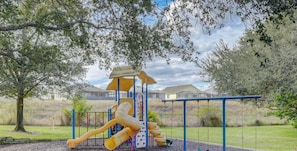 A playground with slides and swings, surrounded by trees and a fence.
