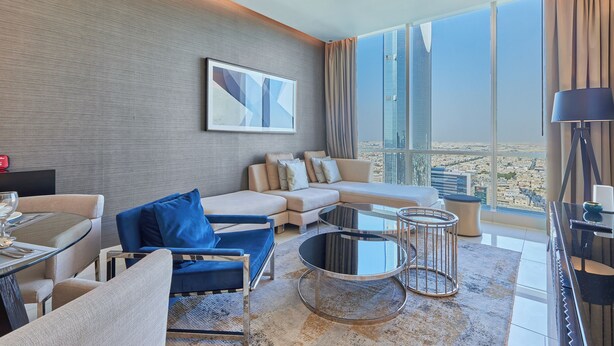 A modern hotel room with a large window, a sofa, a dining table, and a piano. - bnbme | Damac Resi (Riyadh)