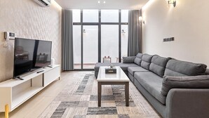 A modern living room with a flat-screen TV, a sofa, a coffee table, and a large window with curtains. - bnbme | Riviera-A5 | 3 Bdr (Riyadh)