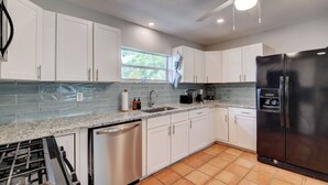 A modern kitchen with white cabinets, a stainless steel refrigerator, and a window providing natural light. - Coastal Cottage private oasis w/ Hot Tub & less than 5 minutes to beach! (Boynton Beach)