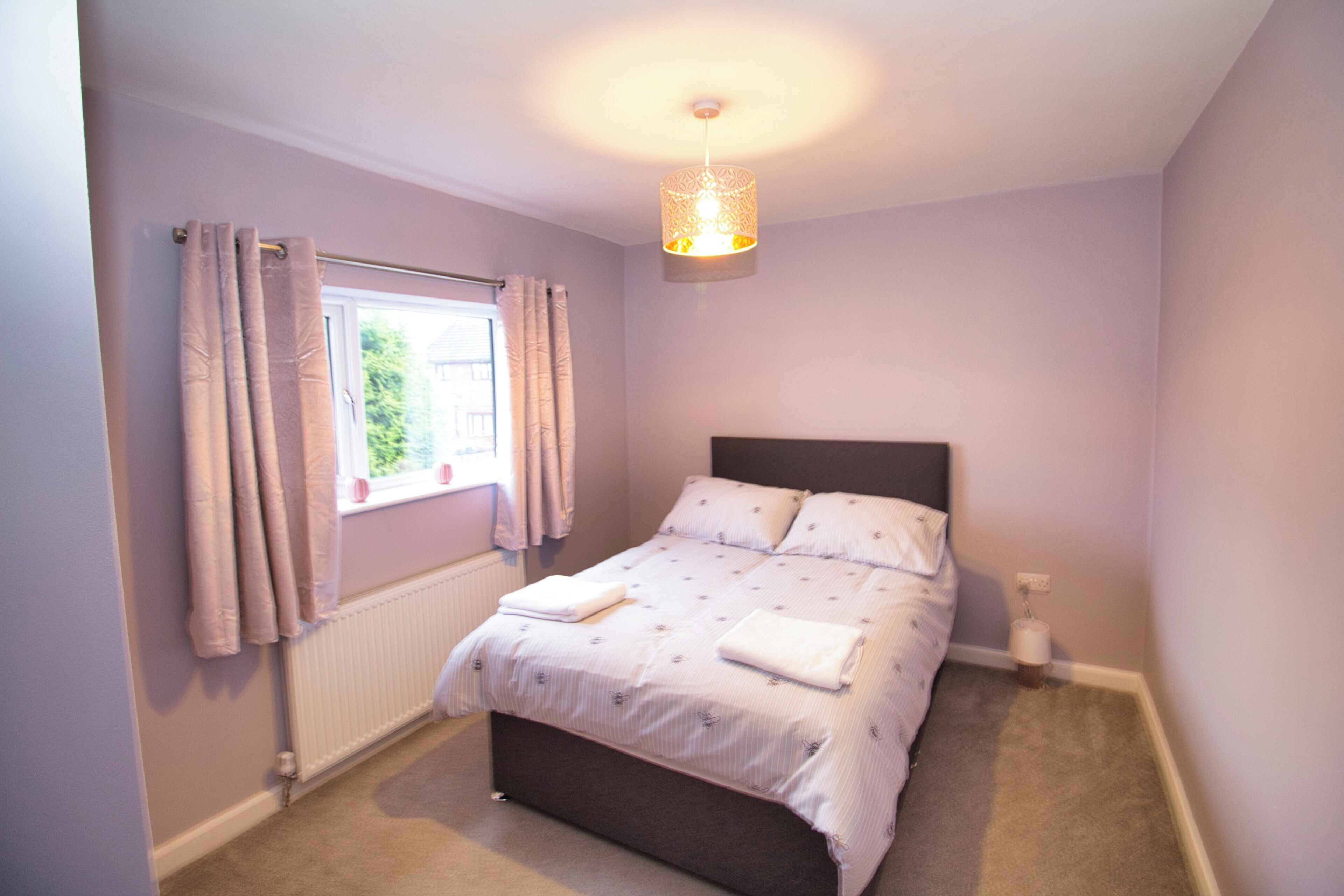 A bedroom with a bed, a window with curtains, a radiator, and a hanging light fixture.