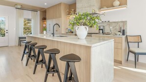 Eine moderne Küche mit einer zentralen Kochinsel, Barhocker, einer Kaffeemaschine und einem Blumentopf.