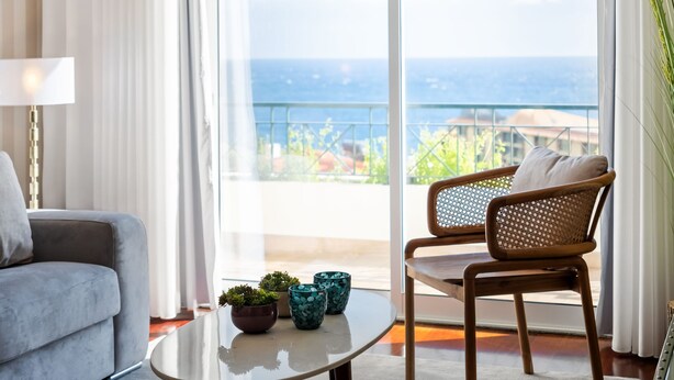 A modern living room with a sofa, a chair, a glass coffee table, and potted plants. - Exquisite Ocean Apartment by Homie (Santa Cruz)