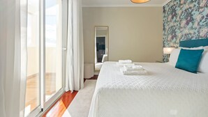 A hotel room with a large bed, a view through the window, a mirror, and a floral wallpaper. - Exquisite Ocean Apartment by Homie (Santa Cruz)
