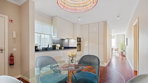 A modern kitchen with a glass dining table and chairs, a fire extinguisher, and a view into the living area. - Exquisite Ocean Apartment by Homie (Santa Cruz)