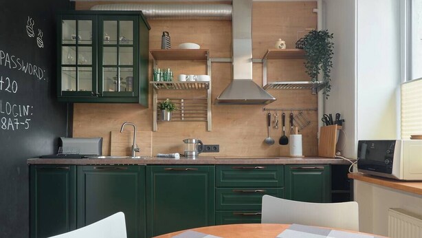Une cuisine moderne avec des meubles de couleur verte, un tableau noir sur lequel est écrit un mot de passe, et une table à manger en bois.