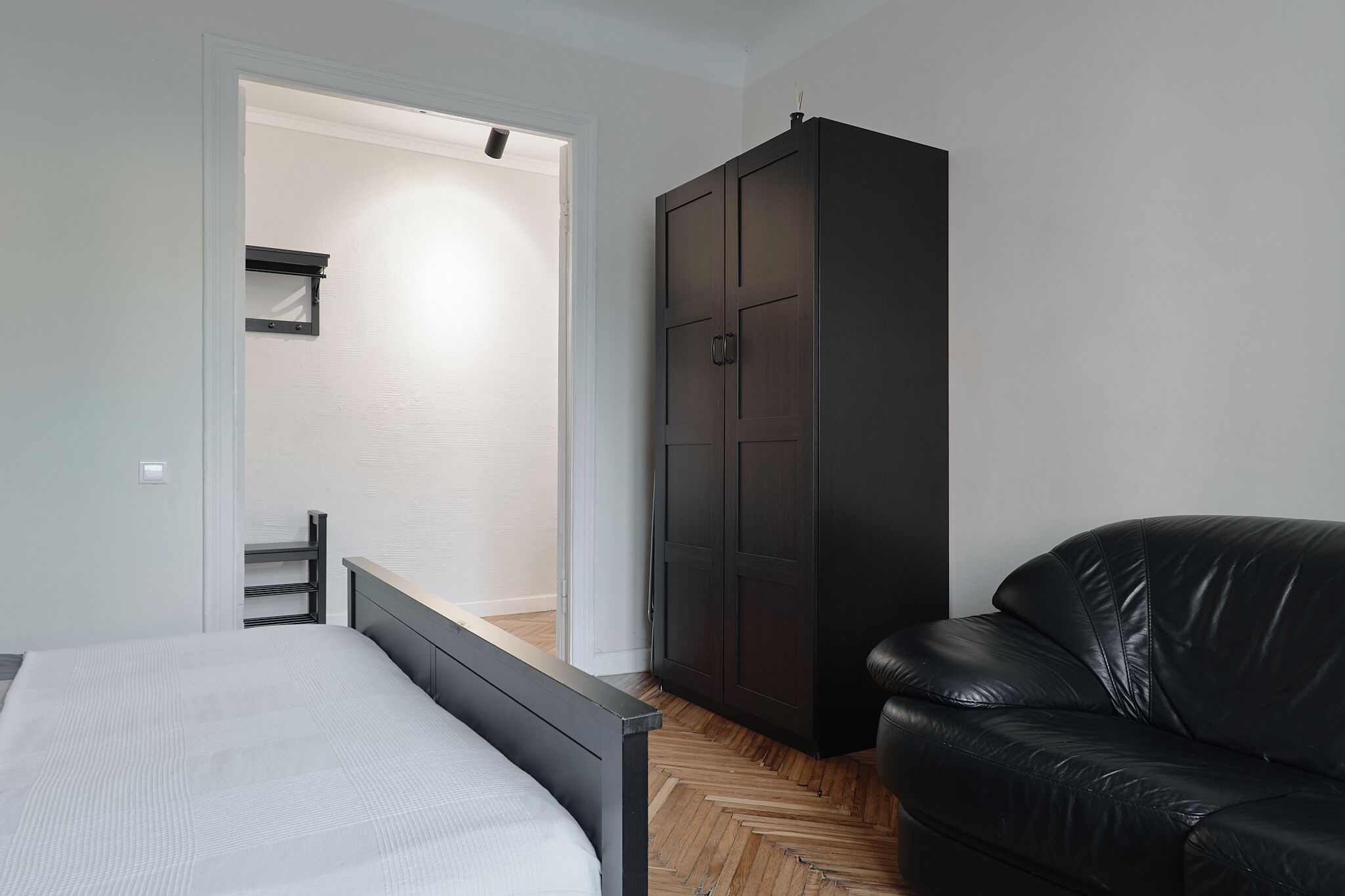 A bedroom with a bed, a wardrobe, and a black leather sofa.
