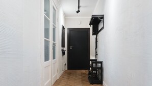 Un couloir doté d’un parquet en bois disposé en chevrons, de murs blancs, d’une porte noire et d’une étagère noire.