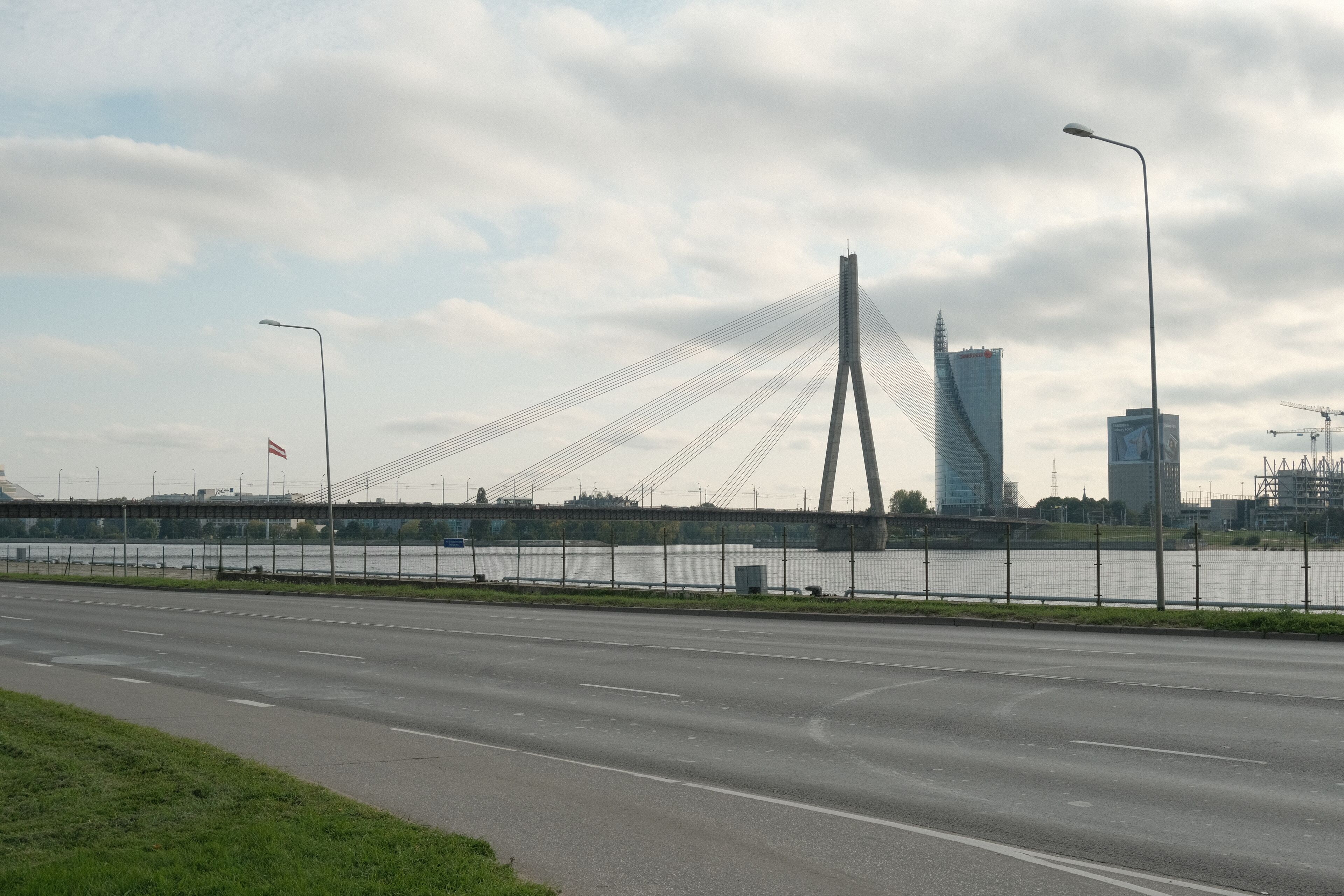 Un pont moderne avec des câbles, une rivière et des bâtiments urbains en arrière-plan.