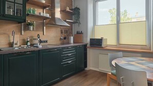 Une cuisine moderne avec des meubles de couleur verte, un plan de travail en bois et une fenêtre équipée de stores.