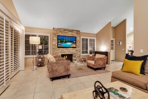 A spacious living room with a stone fireplace, a flat-screen TV mounted above it, and a comfortable seating area with sofas and a coffee table. - Desert Retreat - Walk to Indian Wells Tennis (Palm Desert)
