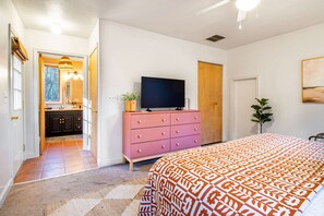 Un dormitorio con una cama grande, un aparador rosa, un televisor de pantalla plana y una puerta de madera.
