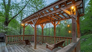 A wooden deck with a pergola, outdoor seating, and string lights.