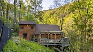 A cabin with a wooden deck and a small porch, surrounded by dense forest.