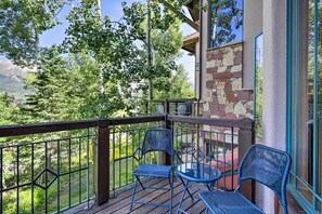 Ein Balkon mit zwei blauen Stühlen und einem kleinen Tisch, mit Blick auf eine gebirgige Landschaft.
