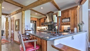 Cucina con travi in legno, isola in marmo e uno sgabello rosso.