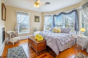 A bedroom with a bed, a chair, a dresser, a lamp, and a window with curtains.