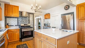 A modern kitchen with wooden cabinets, a stainless steel refrigerator, a built-in oven, and a large island with a sink.