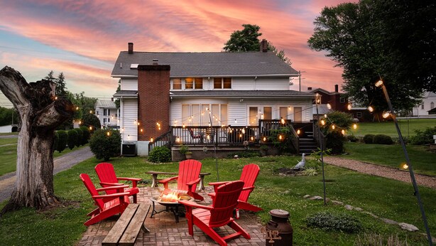 A house with a brick patio, red Adirondack chairs, a fire pit, and string lights.