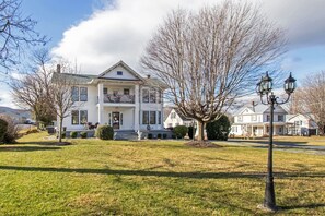 A large white two-story house with a front porch, a small garden, and a street lamp.