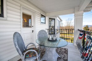 A porch with a glass table and wicker chairs, a metal railing, and a view of the outdoors.
