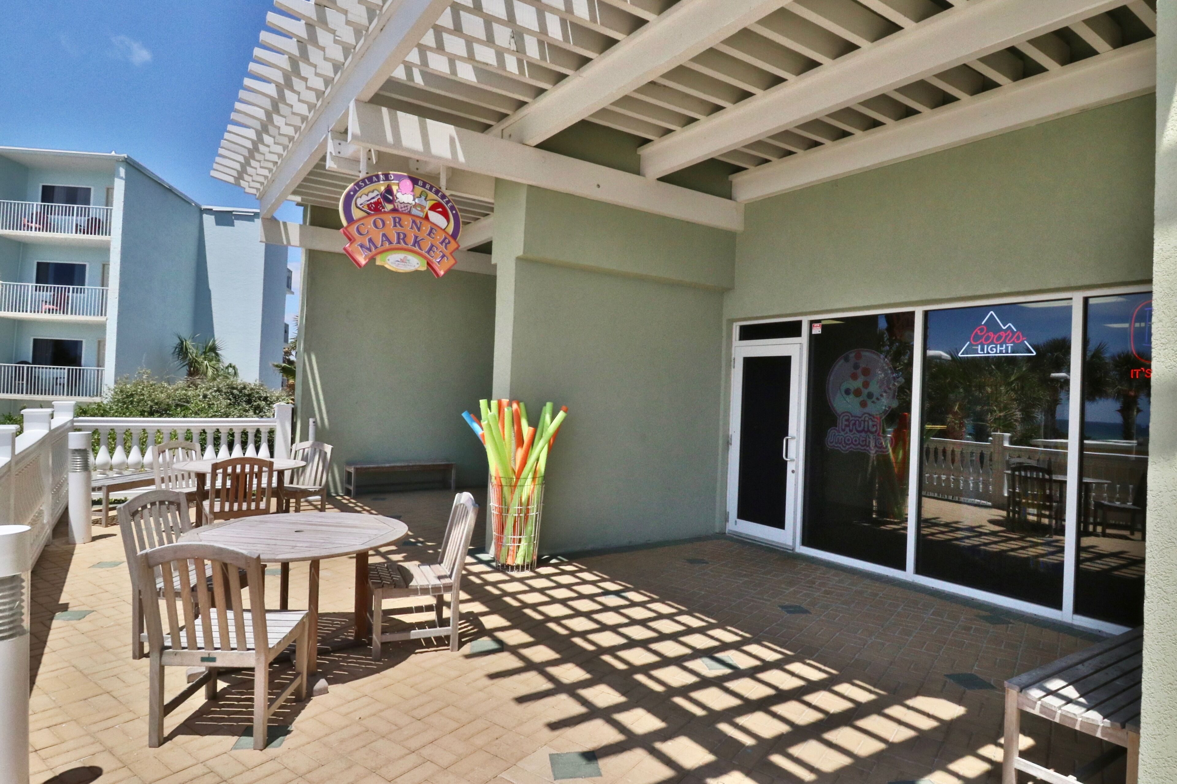 A covered outdoor patio with wooden tables and chairs, a Coors Light sign, and a Coors Light logo on the glass doors.