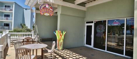 A covered outdoor patio with wooden tables and chairs, a Coors Light sign, and a Coors Light logo on the glass doors.