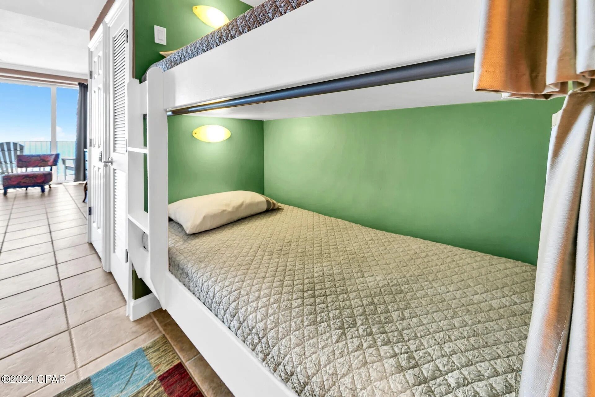 A bunk bed room with green walls, a white ceiling, and a view of the balcony.