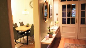 Un coin repas avec une table et des chaises en bois, un miroir, une horloge et une porte ornée de vitraux.