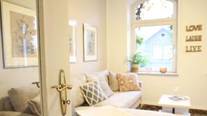 Un salon confortable avec un canapé, des coussins, une petite table et une fenêtre donnant sur une maison.