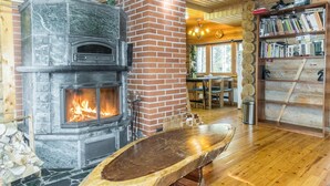 A rustic interior with a stone fireplace, wooden furniture, and a bookshelf. - Peurakangasranta 4 * luxury logcabin in Ranua, lakeside in the forest with AC (Lappi)