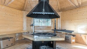 A wooden cabin interior with a central fireplace, a window, and a wooden bench. - Peurakangasranta 4 * luxury logcabin in Ranua, lakeside in the forest with AC (Lappi)