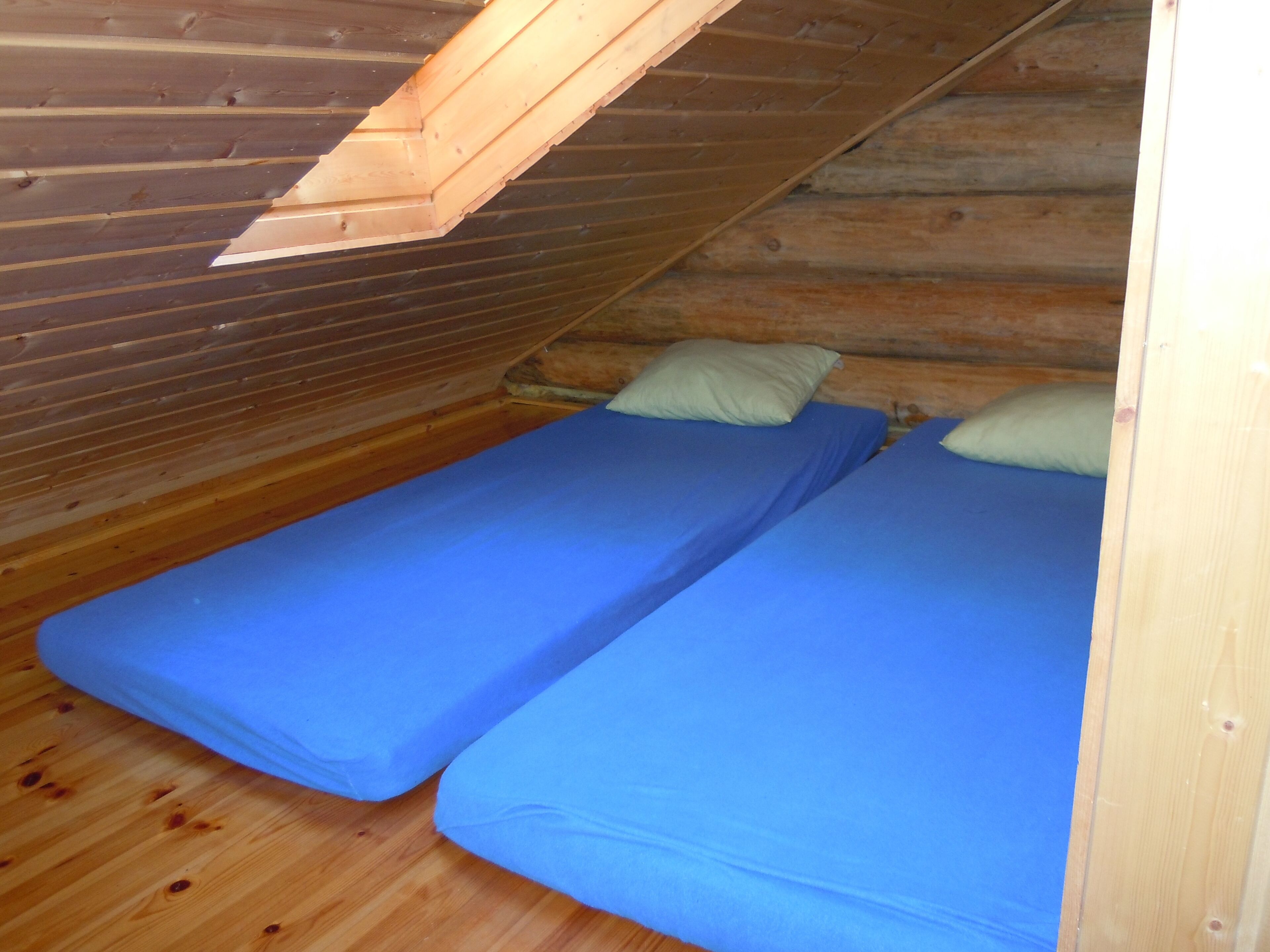 A small, wooden cabin with two single beds, each with a blue mattress and a pillow.