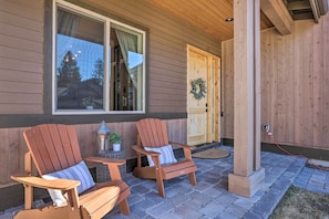 Two wooden Adirondack chairs with cushions, a lantern, and a wreath on a wooden door.