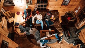 A cozy cabin interior with wooden walls and floors, a fireplace, and a dining area with chairs and a table. - Cabin, Queen Bed, 2 Bunks, Private Bath (Greenville)
