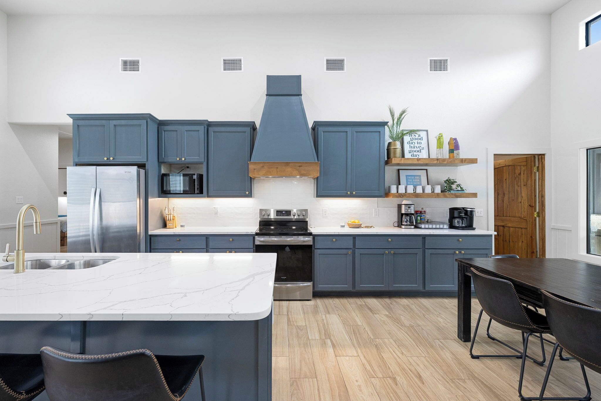 Une cuisine moderne avec des meubles gris, un îlot central, des appareils en acier inoxydable et un plancher en bois.