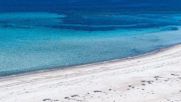 A beach with clear turquoise waters and a sandy shore.